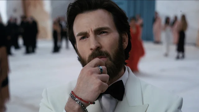 Chris Evans in a white tuxedo at a gala, with guests blurred behind him