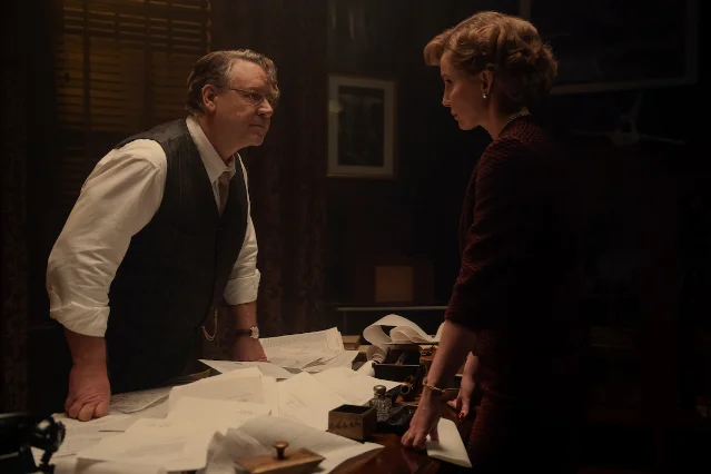 Russell Crowe and Annabelle Wallis facing each other across a desk in a dimly lit office in Unabomber