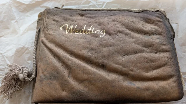 a weathered brown leather wedding album stamped "Wedding" in gold, lying on crumpled tissue paper