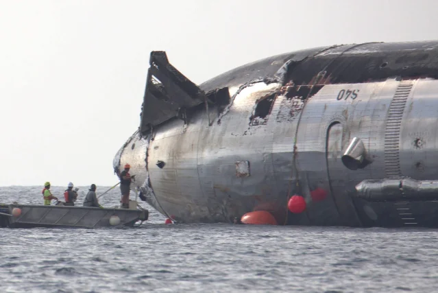 海面上漂浮着一段黑色、受损的圆柱形飞行器结构,旁边有小艇和人员,船体可见「S40」字样