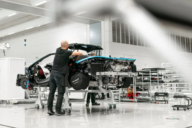 A worker leaning over a partly assembled McLaren chassis in a brightly lit factory