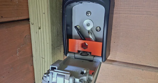 Orange 3D-printed organizer insert fitted inside an open wall-mounted key lock box, with keys visible in the compartment