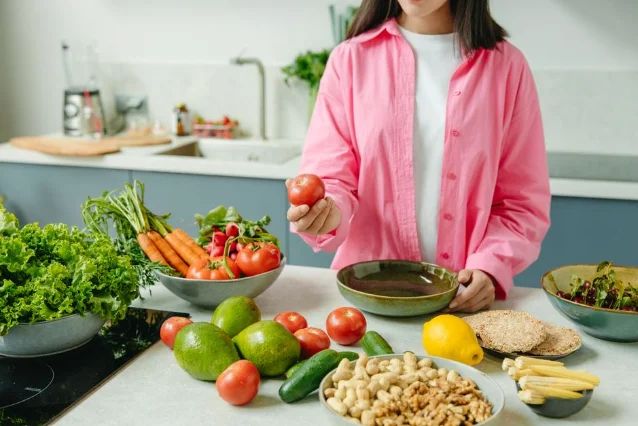 Person preparing a spread of fresh vegetables and fruit at a kitchen counter