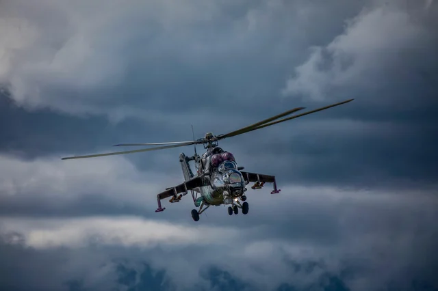 A military helicopter moves through overcast skies