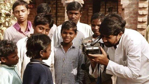 A man films children as Kailash Satyarthi stands among them in India.