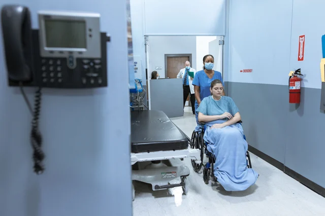 Nurse assisting a patient in a wheelchair through a hospital corridor
