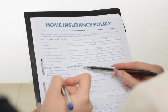 Hands filling out an insurance policy claim form on a desk