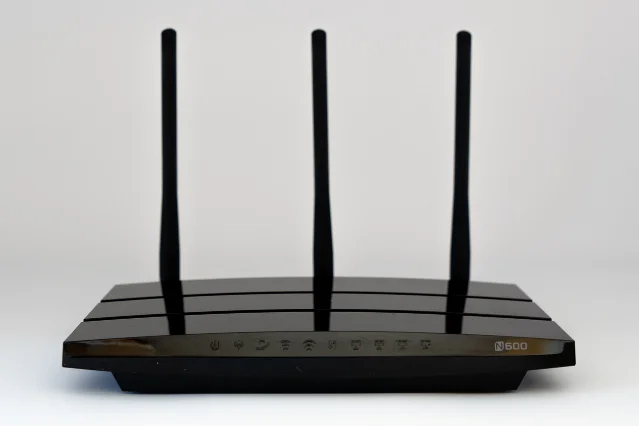 A black wireless router with three antennas on a white surface