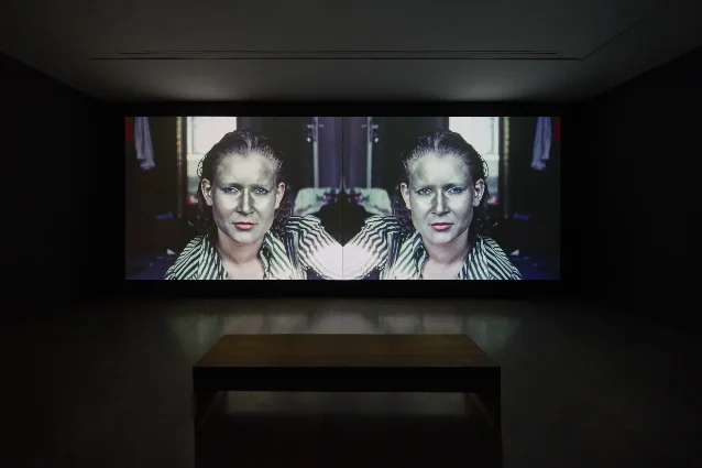 柏林画廊里双通道放映的黑色展厅，屏幕上是镜像对称的人脸