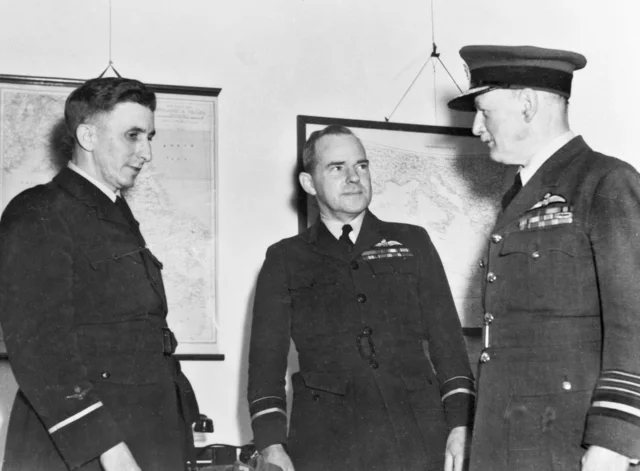 Three officers in uniform standing together in front of framed wall maps