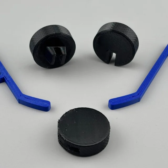 Two black puck-shaped clips and blue hockey-stick brim clips displayed on a white surface