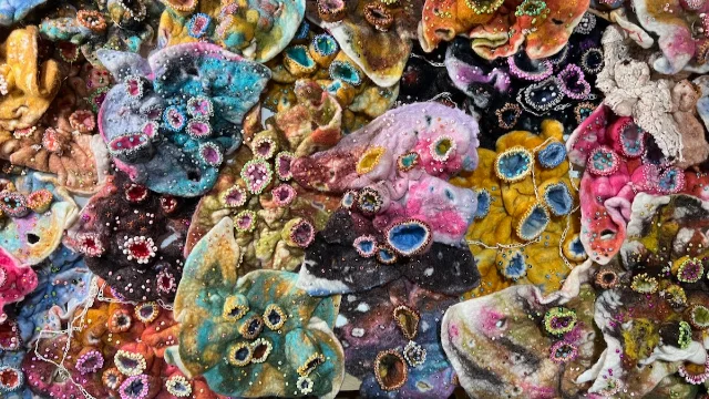 Hand-felted wall-sized artwork representing the intestinal microbiome, with embroidered bacterial forms and deliberate holes depicting antibiotic dysbiosis.