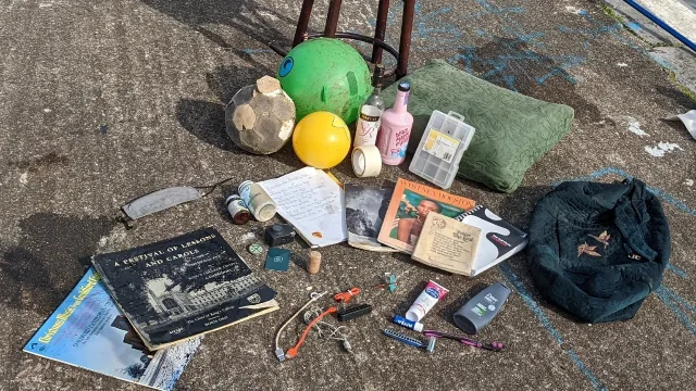 An assortment of objects recovered from Bristol Harbour laid out on concrete: footballs, an inflatable, glass bottles, a pillow, a record sleeve, a book and cables