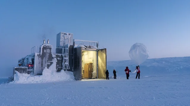 People in cold-weather gear inflate a large balloon outside a snow-covered building