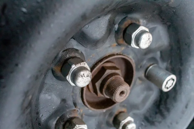The bare hub of a car wheel with four threaded studs, three lug nuts visible, and the large centre axle nut, with the brake assembly behind