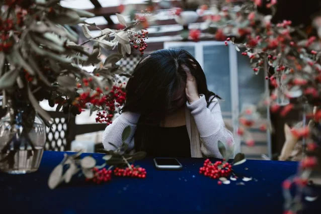 Woman with head in hands at a table, phone in front of her — the aftermath of checking and rechecking with no reply