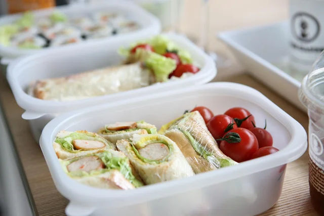 Two open lunch containers on a table: one holds cut sandwich rolls and cherry tomatoes, the other a salad
