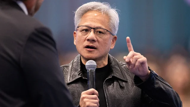 Jensen Huang speaking into a microphone with one finger raised, wearing a black leather jacket, at Salesforce's Dreamforce conference.