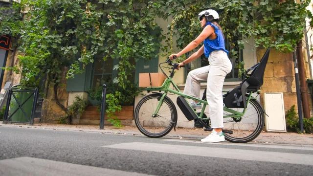 Woman in helmet riding a green eBike along a Paris street