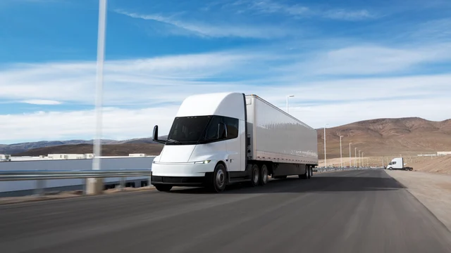 A white Tesla Semi with a box trailer running on a desert highway, mountains behind