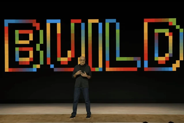 Satya Nadella 站在 Build 2026 舞台，身后黑色背景显示彩色像素风格 BUILD 文字