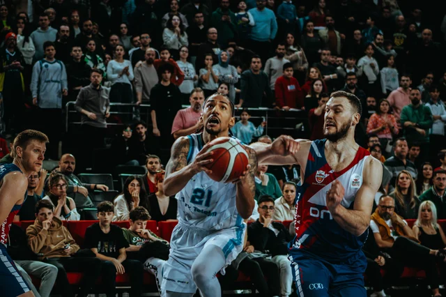 Basketball players contesting a drive in a crowded indoor arena