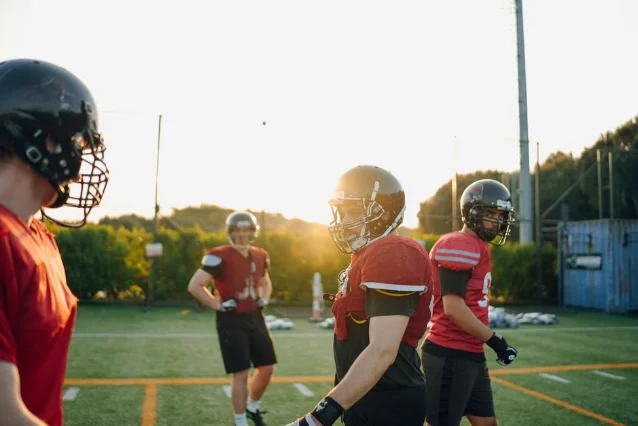 Football players in helmets and practice gear during a sunset field session, standing between drills