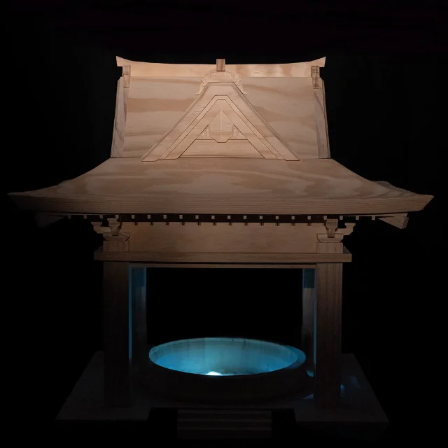A pale wooden shrine-like pavilion with a circular blue-lit basin beneath its raised floor