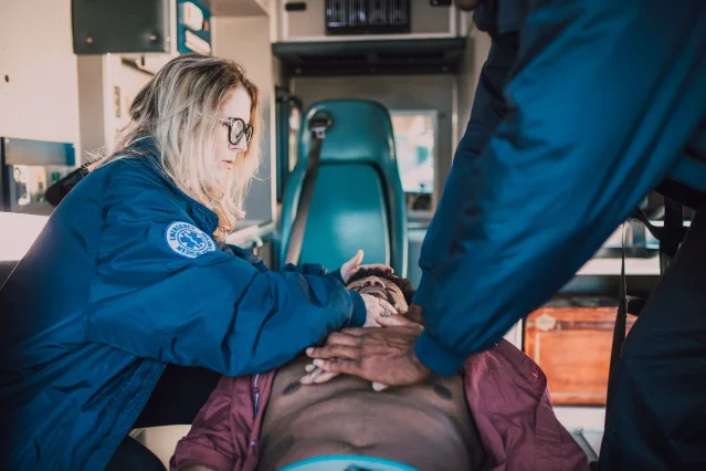 Two paramedics performing CPR on a patient in an ambulance, with one pressing on the patient's chest