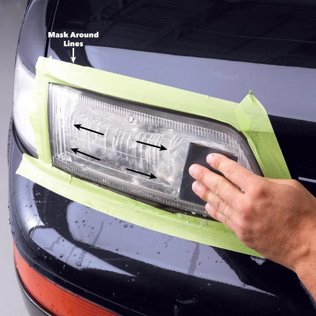 A rectangular headlight on a dark car, masked off in green tape and printed with the words "Mask Around Lines", as a bare hand sands the wet lens with a dark block in straight horizontal passes marked by printed arrows