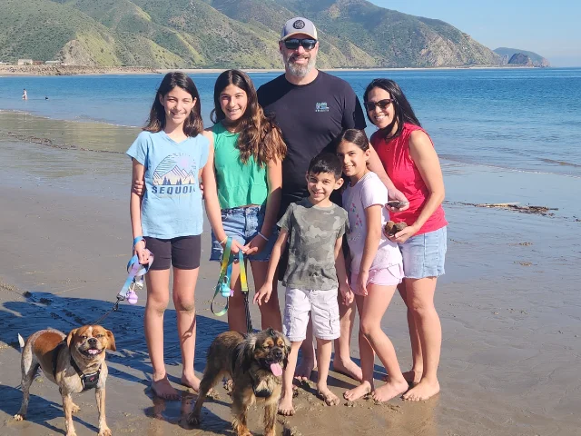 Six members of the Patton family stand with two dogs on a beach.