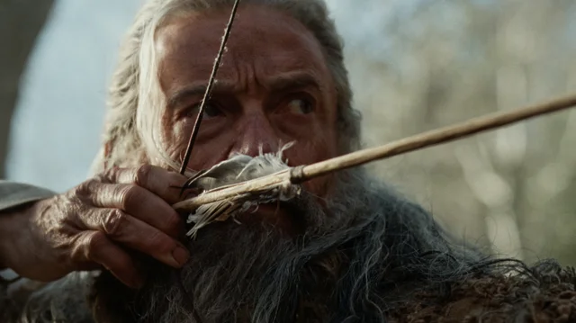 Hugh Jackman as Robin Hood, drawing a bow, arrow at his cheek