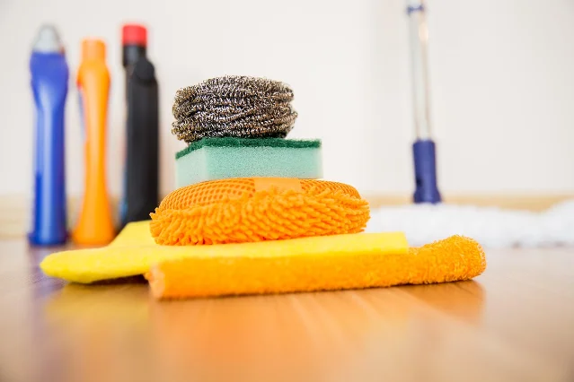 Cleaning cloths, scrubbers, brushes, and bottles arranged on a wooden surface.