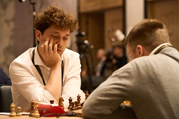 A player resting his chin on his hand at a chessboard, with his opponent's back in the foreground