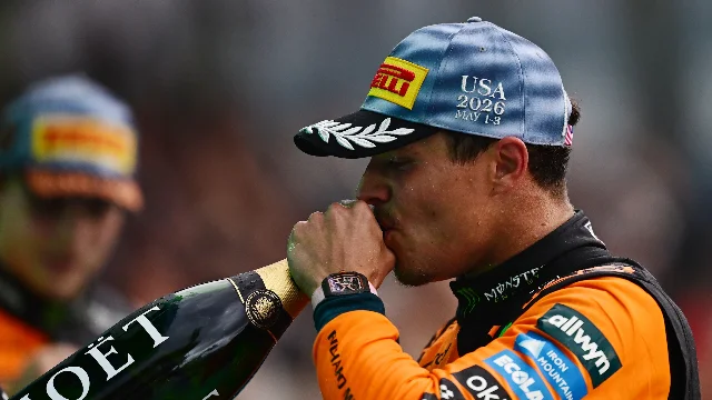 Lando Norris drinks champagne on the Miami GP podium, McLaren cap and race suit on