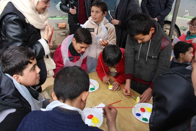 Children draw and paint beside the Mobile Cultural Bus at a Syrian camp.
