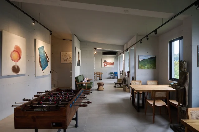 清水混凝土的展厅里挂着多幅画作,前景是一台木制桌上足球台