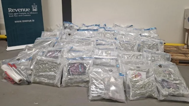 Dozens of transparent plastic bags containing seized cannabis, stacked on a warehouse floor, with a Revenue — Irish Tax and Customs banner visible on the left