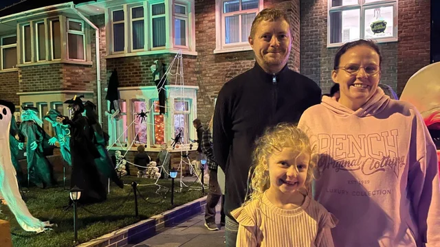 a family at night in front of a lit house decorated with witches, cobwebs and inflatable figures