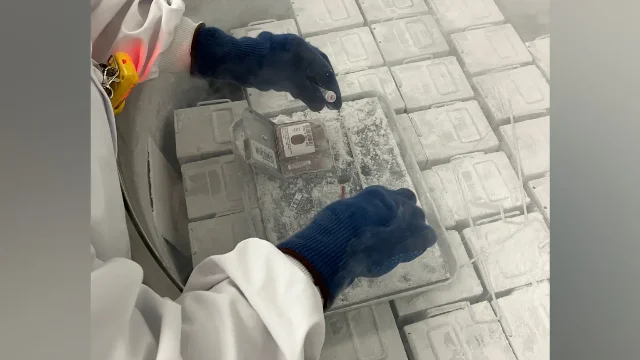 A gloved hand lifting a small sample vial from a cryogenic freezer packed with frost-covered storage boxes.