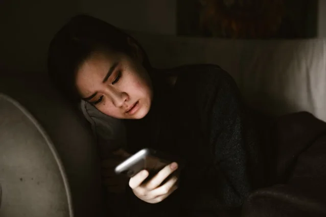 暗光下女生抱手机追剧