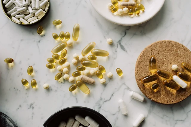 Assorted supplement capsules, powders, and gelcaps arranged in bowls and on a marble surface with cork coasters
