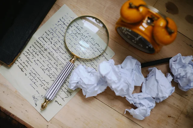 A magnifying glass rests on a handwritten letter surrounded by crumpled paper and an old clock — evoking archival correspondence and letters from the past