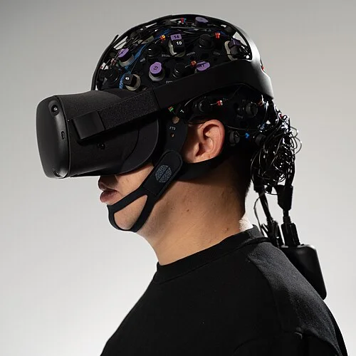 Two participants wearing wireless fNIRS and EEG headsets side by side, illustrating a hyperscanning setup for social neuroscience