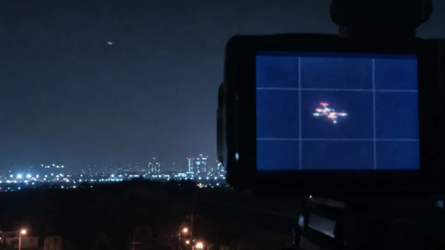 目击者手持相机对准夜空拍摄,相机屏幕显示多色异常光点