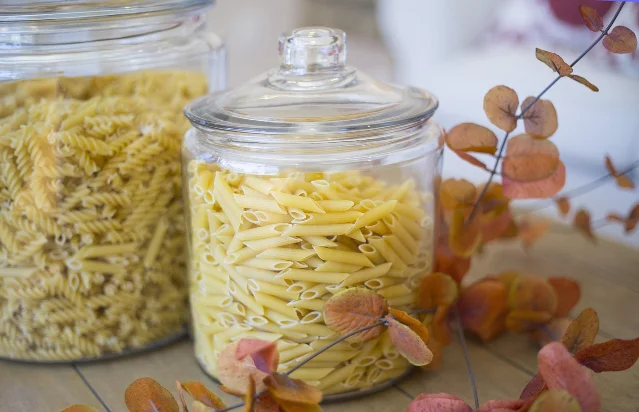 Two glass jars holding different shapes of dry pasta