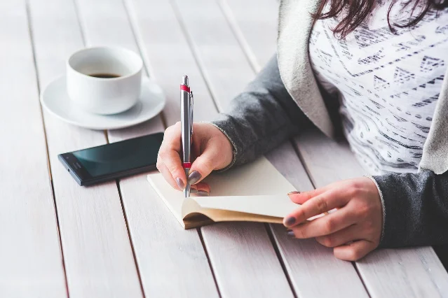 Student at a desk writing notes with a notebook and pen