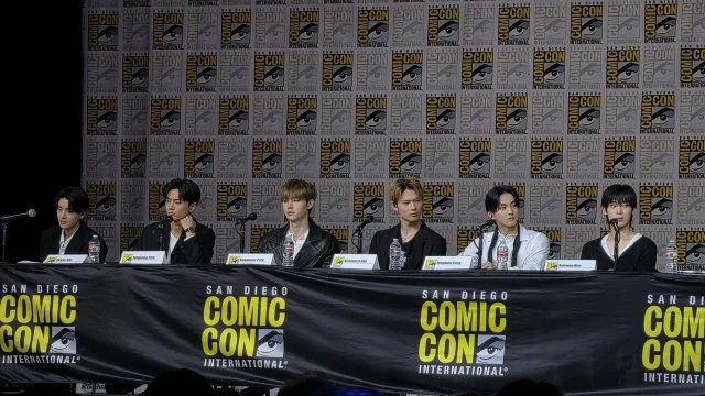 ENHYPEN 六名成员坐在圣迭戈 Comic-Con 采访桌后，背景是 Comic-Con 标识墙