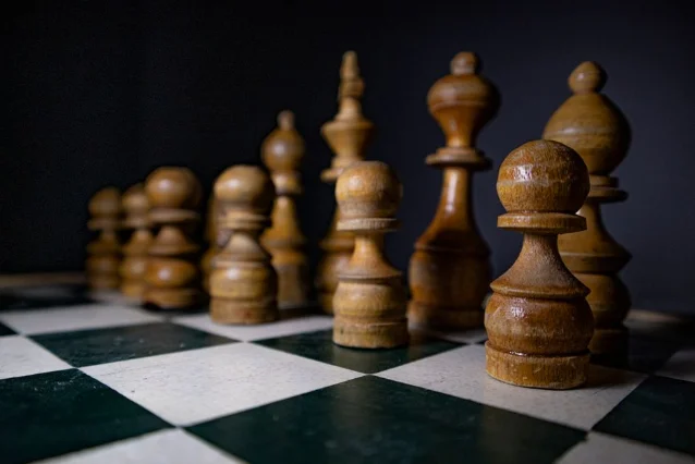 Wooden chess pieces on a green-and-white board — patience before the decisive move