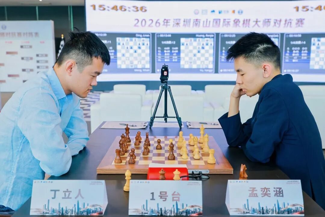 Ding Liren and Meng Yihan at their board in a bright hall, with live game screens and Chinese event signage behind them